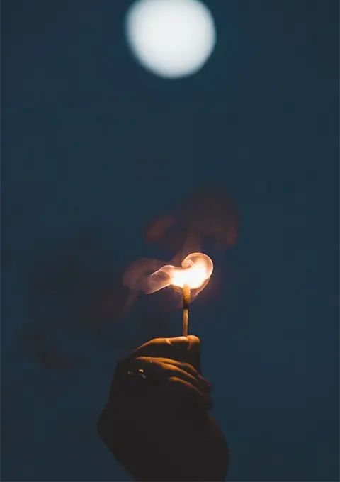 Hand holding a burning fire stick used in powerful good luck spell rituals